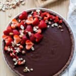 A whole chocolate tart with heart-shaped strawberry pieces on top.